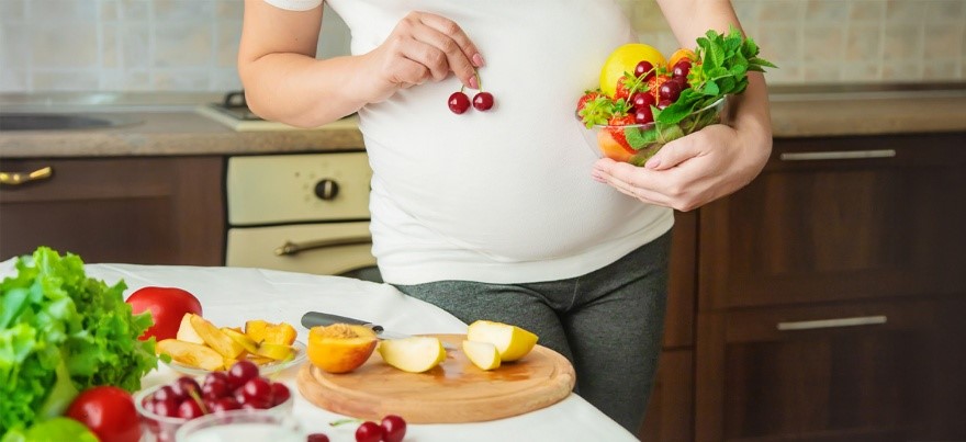 Pregnant woman holding a bowl of fresh fruits and vegetables, promoting healthy foods to eat during pregnancy – BirthRight by Rainbow Hospitals
