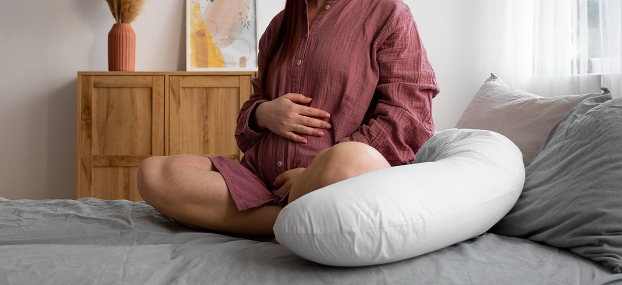 Pregnant woman relaxing on bed with maternity pillow while preparing for painless delivery at BirthRight by Rainbow Hospitals.