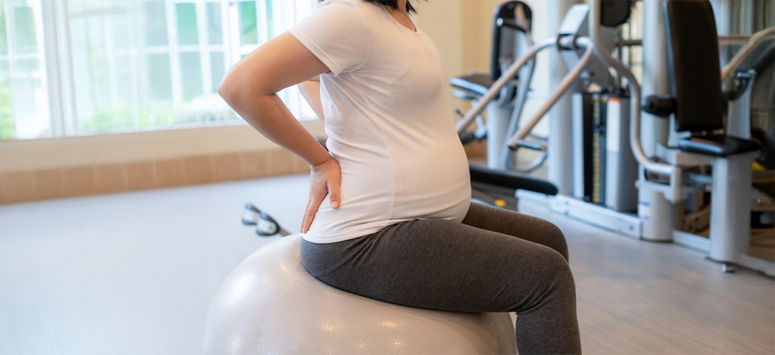 Pregnant woman doing back pain relief exercises on a gym ball under physiotherapist guidance — BirthRight by Rainbow Hospitals.