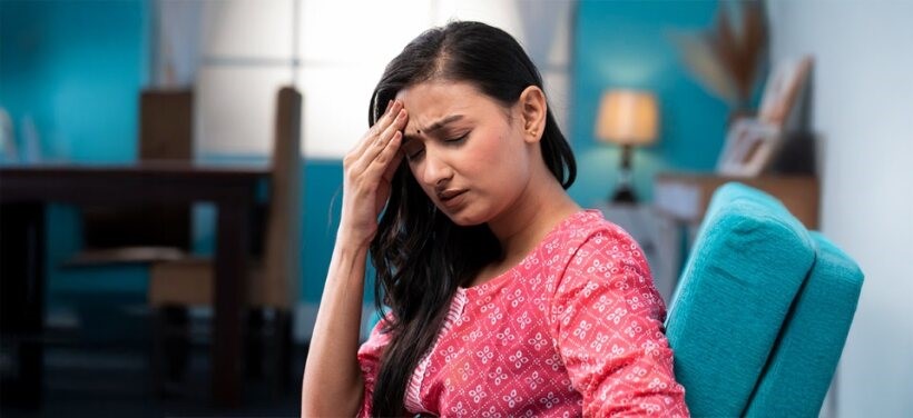 Young woman holding her head in discomfort, showing signs of low estrogen – causes, symptoms, and natural remedies