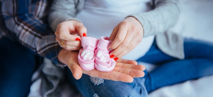 Pregnant woman holding pink baby shoes with her partner, symbolizing hope and preparation for childbirth — BirthRight by Rainbow Hospitals.