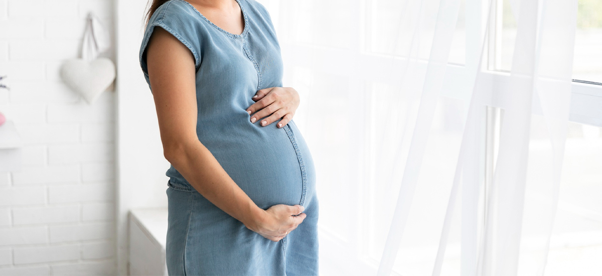 Pregnant woman holding her belly and standing near a window — PCOS pregnancy awareness